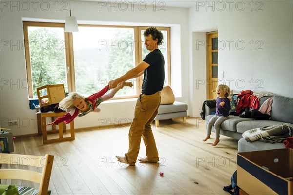 Caucasian father spinning daughter by arm and leg in livingroom