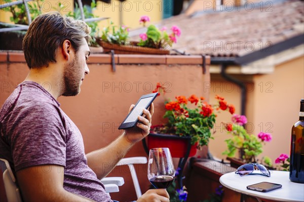 Caucasian man reading digital tablet drinking red wine