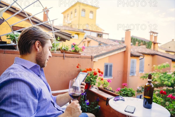 Caucasian man reading digital tablet drinking red wine