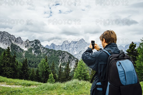 Caucasian man photographing mountain range with cell phone