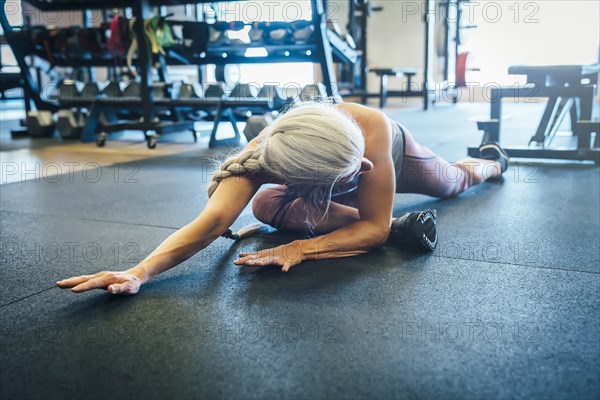 Caucasian woman stretching on gymnasium floor