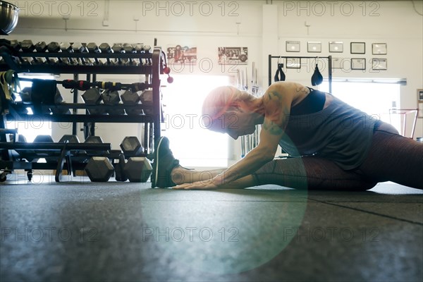 Caucasian woman stretching leg on gymnasium floor