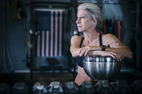 Pensive Caucasian woman leaning on bowl in gymnasium