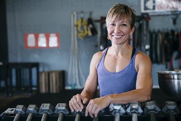 Smiling Caucasian woman leaning on rack in gymnasium