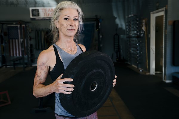Caucasian woman holding large weight in gymnasium