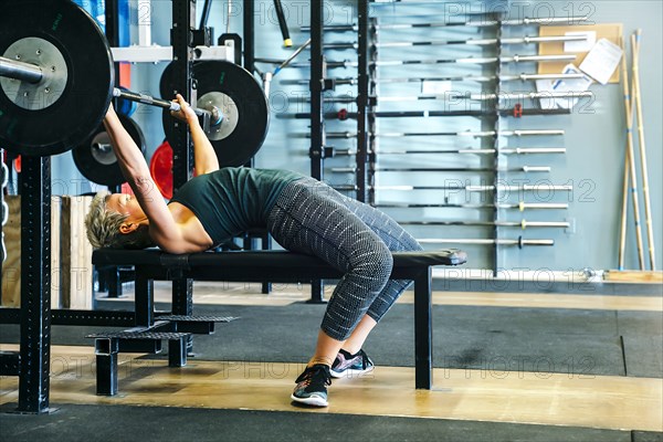 Caucasian woman lifting barbell on bench in gymnasium