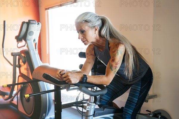 Caucasian woman riding stationary bicycle in gymnasium