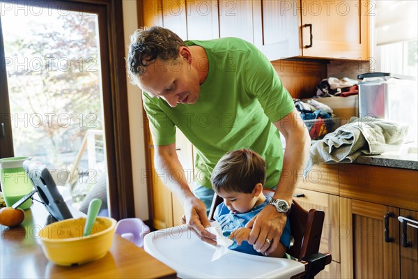 Father wiping hands of son in highchair