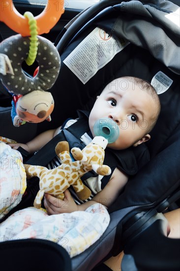Curious Mixed Race baby boy with pacifier in car seat