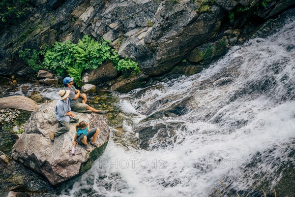 Caucasian people sitting on rock watching river rapids