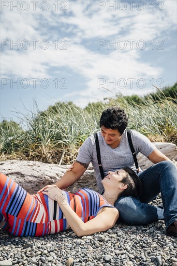 Pregnant lesbian couple relaxing on rocky beach