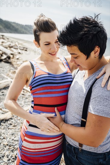 Pregnant lesbian couple hugging on beach