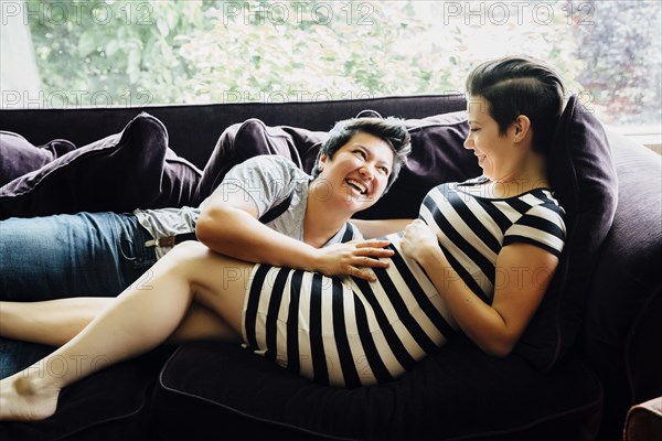 Pregnant lesbian couple cuddling on sofa