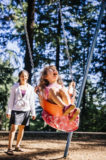 Caucasian mother pushing daughter on playground swing
