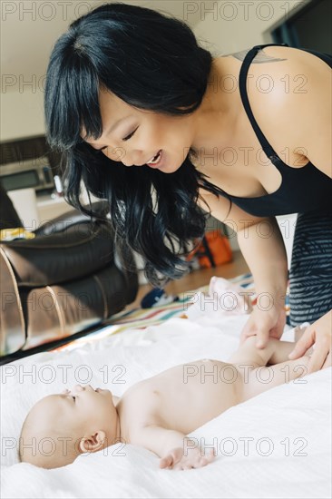 Mother playing with naked baby daughter on blanket