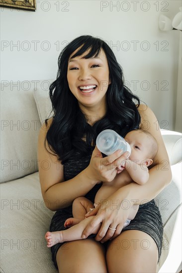 Portrait of smiling mother feeding bottle to baby daughter