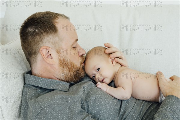 Father laying on sofa kissing baby daughter on head