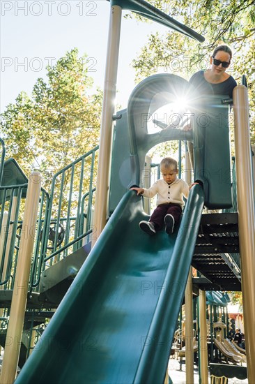 Mother watching son on playground slide