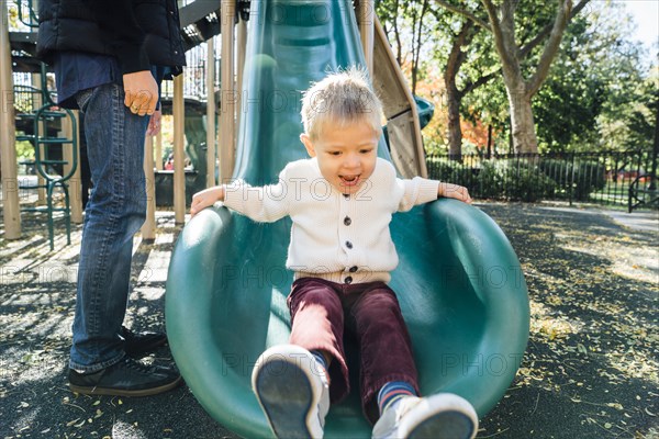 Mixed Race father watching son on playground slide