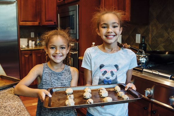 Mixed Race girls holding tray with cookie dough in domestic kitchen