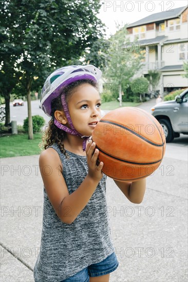 Mixed Race girl wearing helmet playing basketball in driveway