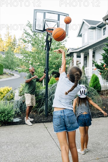 Father and daughters playing basketball in driveway