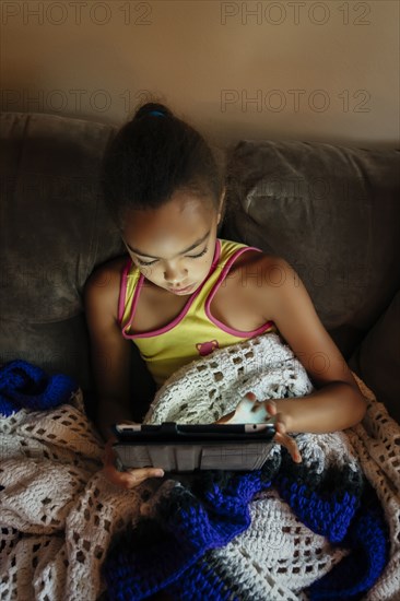 Mixed Race girl using digital tablet on sofa at night