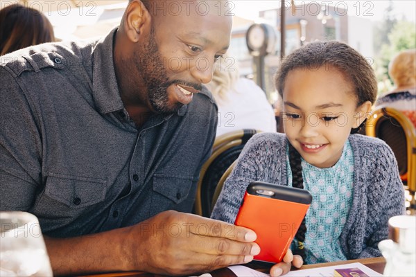 Father and daughter sitting at restaurant table texting on cell phone