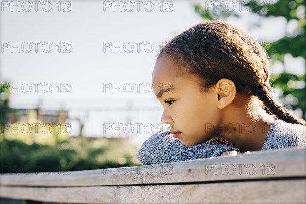 Pensive Mixed Race girl leaning on wooden railing