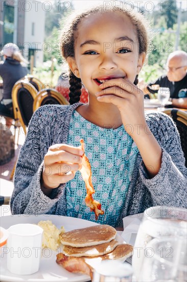 Smiling Mixed Race girl eating breakfast at restaurant