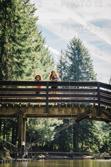 Mixed Race sisters fishing on bridge over river