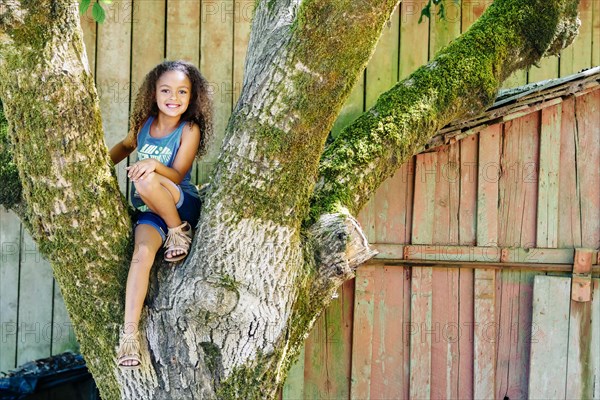 Mixed Race girl sitting in tree