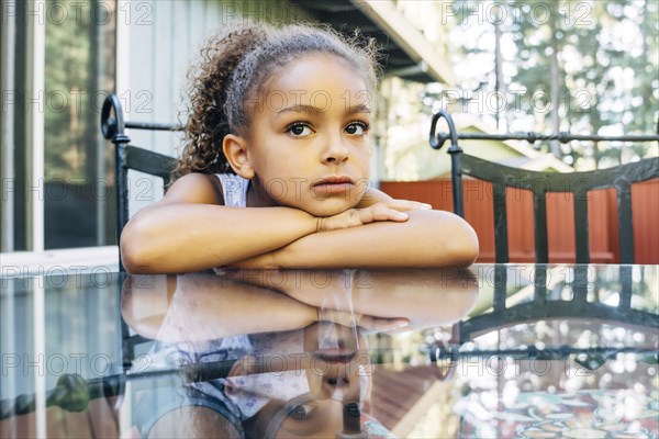 Pensive Mixed Race girl leaning on glass table