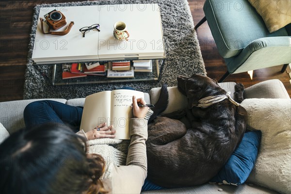 Mixed Race woman on sofa with dog writing in journal