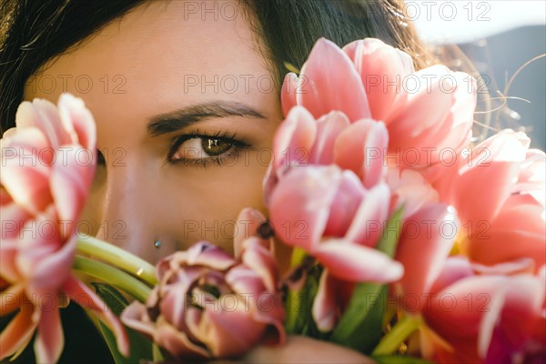 Mixed Race woman hiding face behind flowers