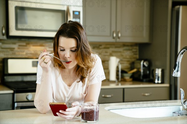 Woman eating smoothie and texting on cell phone