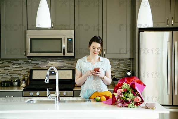 Woman texting on cell phone in domestic kitchen