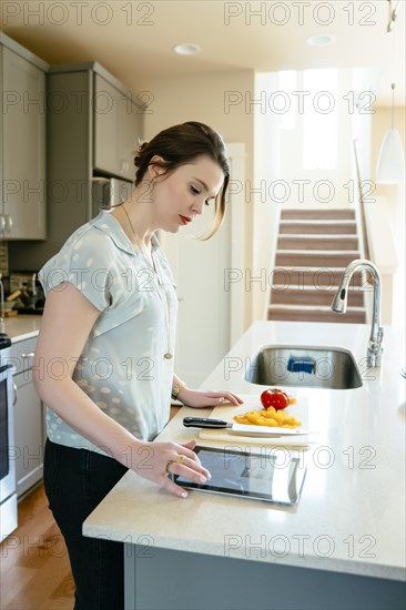 Woman using digital tablet and chopping food in domestic kitchen