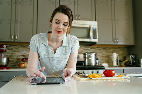 Woman using digital tablet and chopping food in domestic kitchen