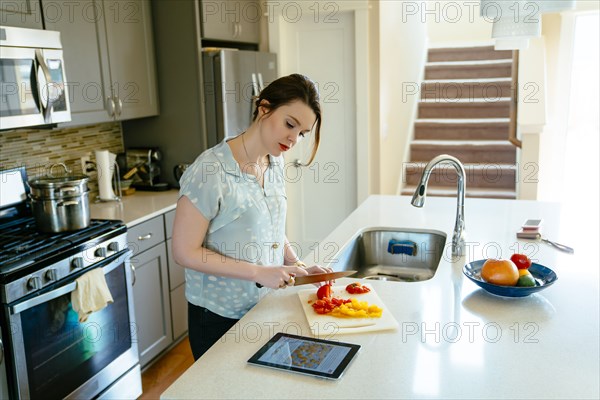 Woman using digital tablet and chopping food in domestic kitchen