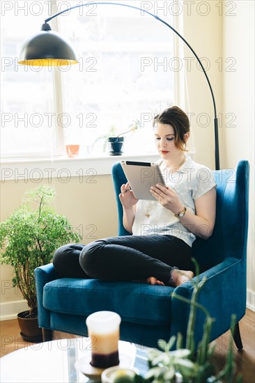 Woman sitting in armchair using digital tablet