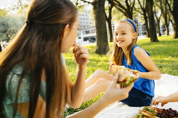 Smiling Caucasian sisters eating food at picnic