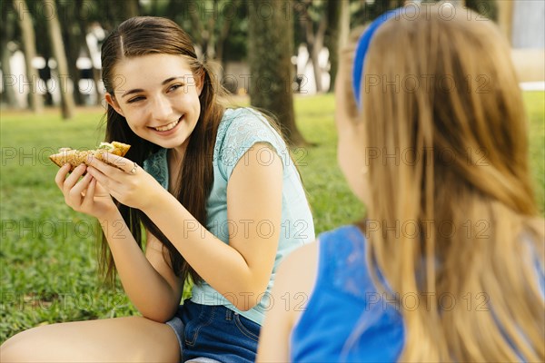 Smiling Caucasian sisters eating food at picnic