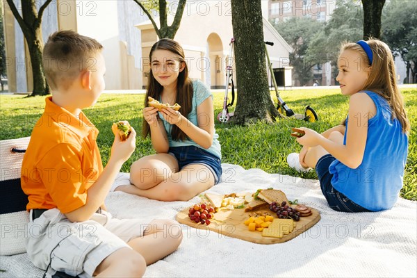 Smiling Caucasian brother and sisters eating food at picnic