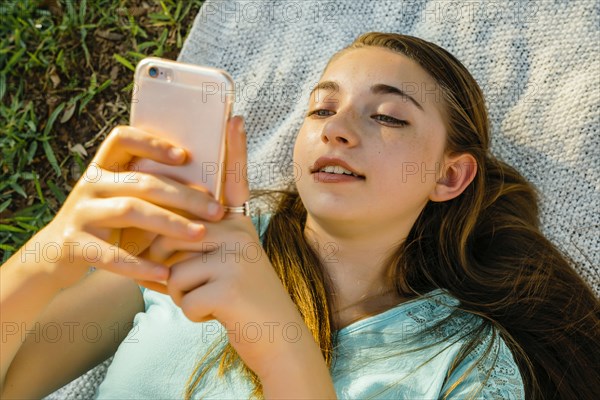 Caucasian girl laying on blanket texting on cell phone