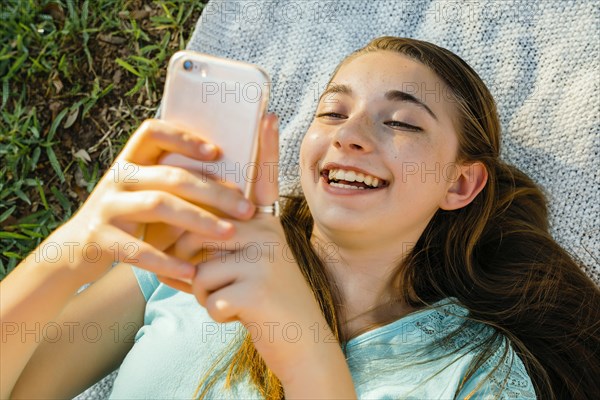 Laughing Caucasian girl laying on blanket texting on cell phone