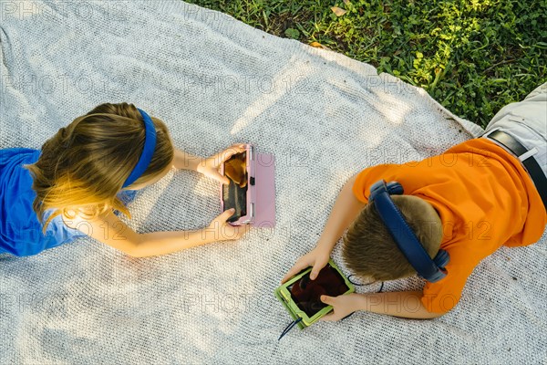 Caucasian brother and sister laying on blanket using technology