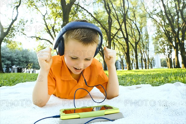 Caucasian boy celebrating on blanket in park with digital tablet