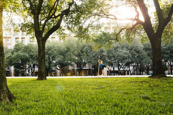 Distant Caucasian girl riding scooter in park