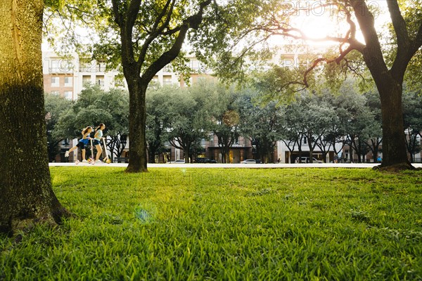 Distant Caucasian girls riding scooter in park